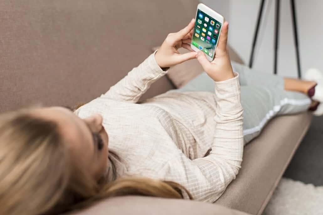 woman on couch using smartphone with ios apps on screen