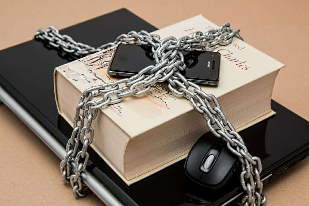 A phone, book, computer, and laptop secured in chains to represent having a disaster recovery plan for securing data and restoring systems and networks