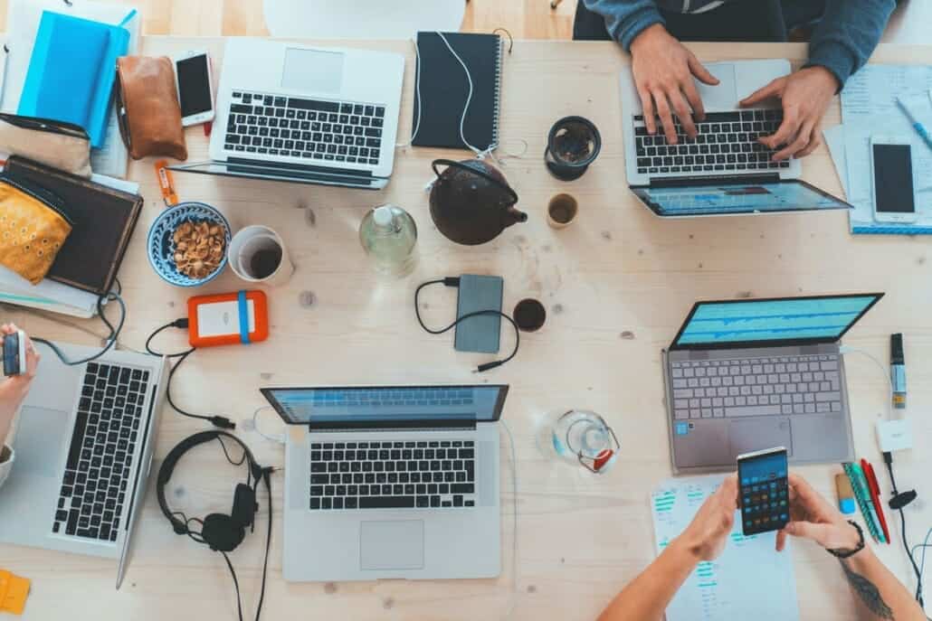 Multiple laptops and devices laid out on a table in a chaotic fashion to represent needing a tech break