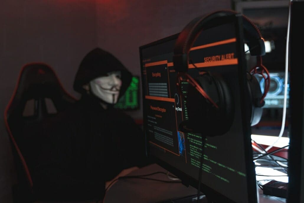 Person in a mask hacking and phishing using their computers which have hacking code on them.
