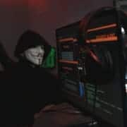 Person in a mask hacking and phishing using their computers which have hacking code on them.