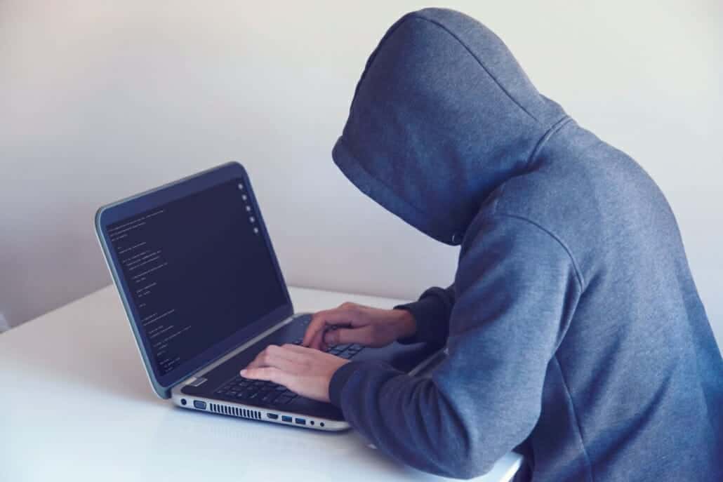 A hacker working on their laptop with a hoodie on, one of the reasons you need to know Threat Intelligence and how it can help you.