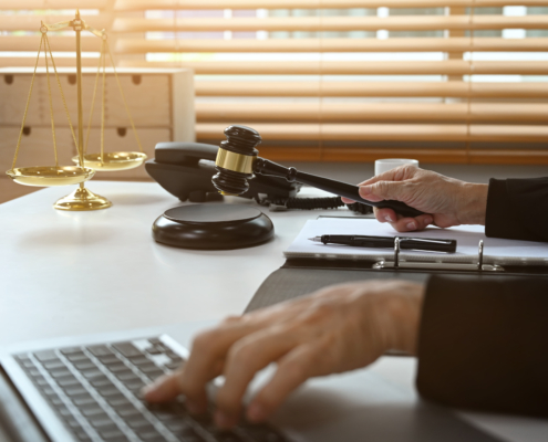 Judge holding a gavel while working on a laptop at her desk with scales of justice in the background