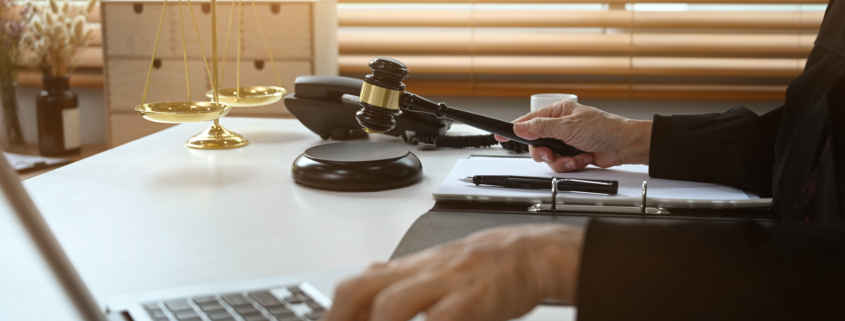 Judge holding a gavel while working on a laptop at her desk with scales of justice in the background
