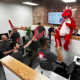 Bastionpoint Technology team members cheering with red foam swords around a red dragon mascot in the office