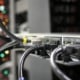 Close-up of cables connected to server equipment, with green status lights and blurred multicolored indicator lights in the background.